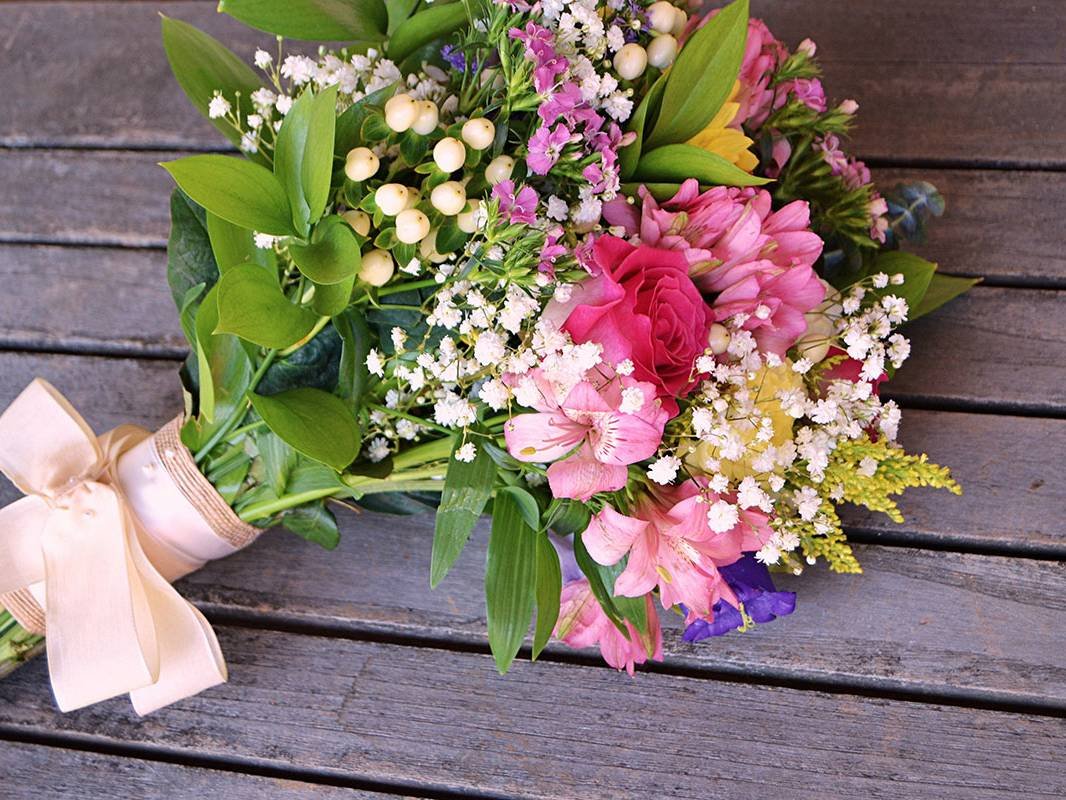 Ramo de flores coloridas con lazo de cinta crema sobre mesa de madera